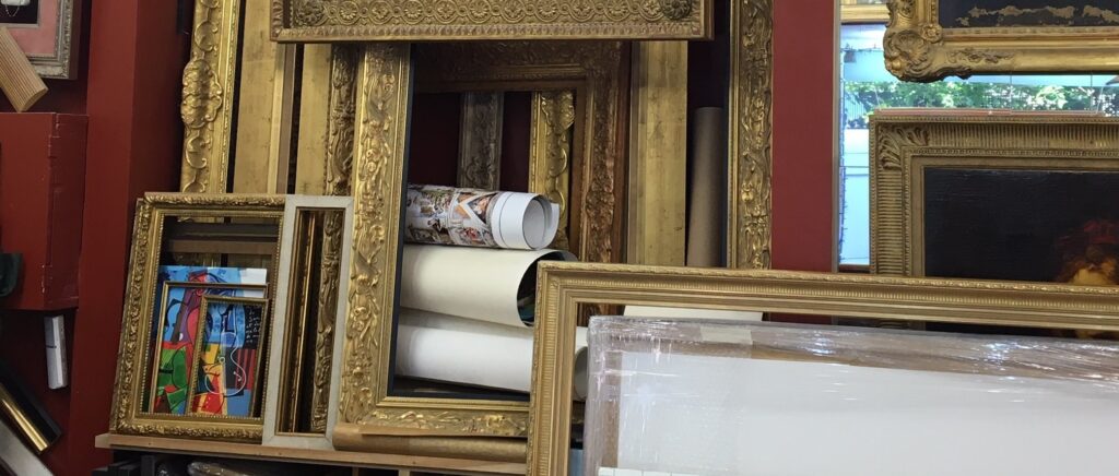 Cadres dorés anciens et rouleaux d’œuvres en attente dans l’atelier