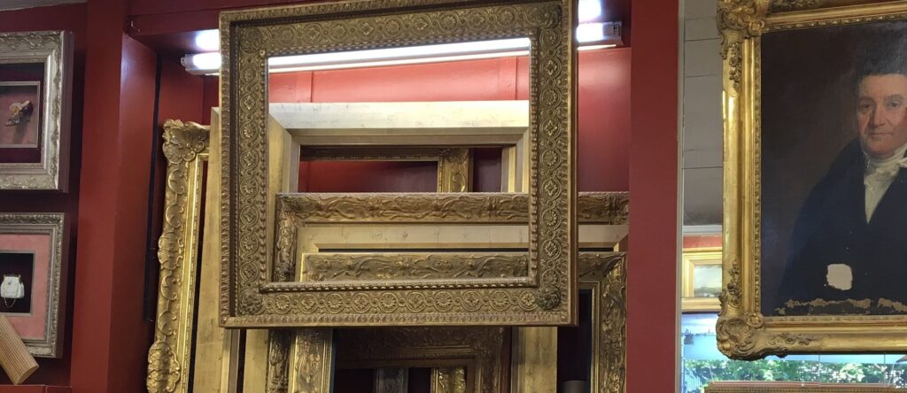 Cadres dorés anciens réunis à l’atelier devant un mur rouge, avec un portrait encadré