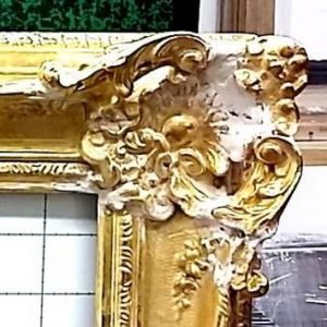 Angle d’un cadre doré sculpté : l’apprêt blanc apparaît là où la dorure manque