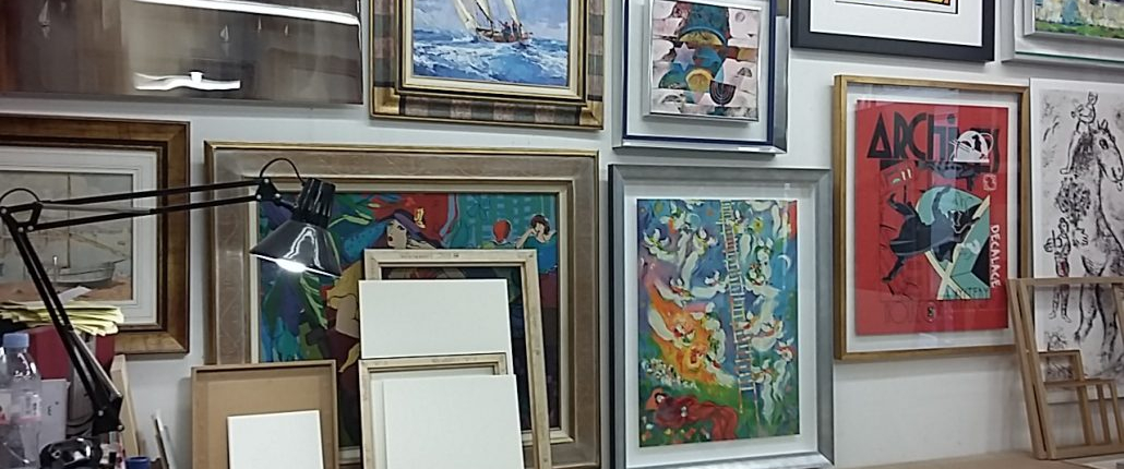Vue de l’atelier : œuvres encadrées, lampe de travail et cadres en préparation